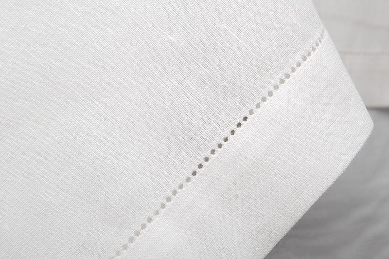Close-up of the hemstitched border and woven texture of a white linen tablecloth.