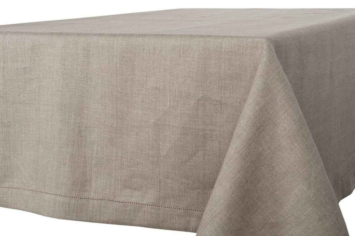 Undyed natural linen tablecloth draped over a rectangular table, showing its woven texture and hemstitched border.