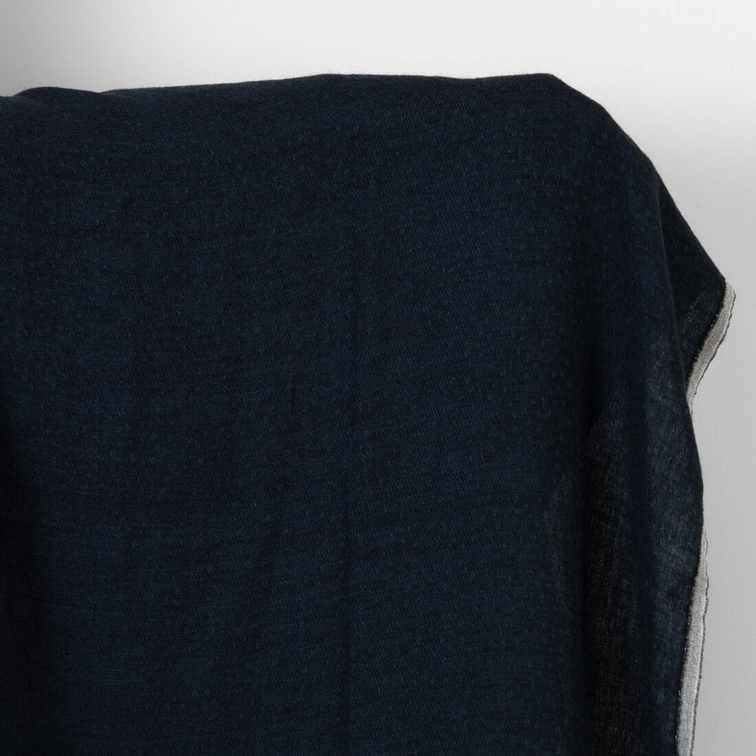 A close-up of a dark navy blue textured fabric draped over a surface, showing its fine woven texture and a thin light-colored edge.