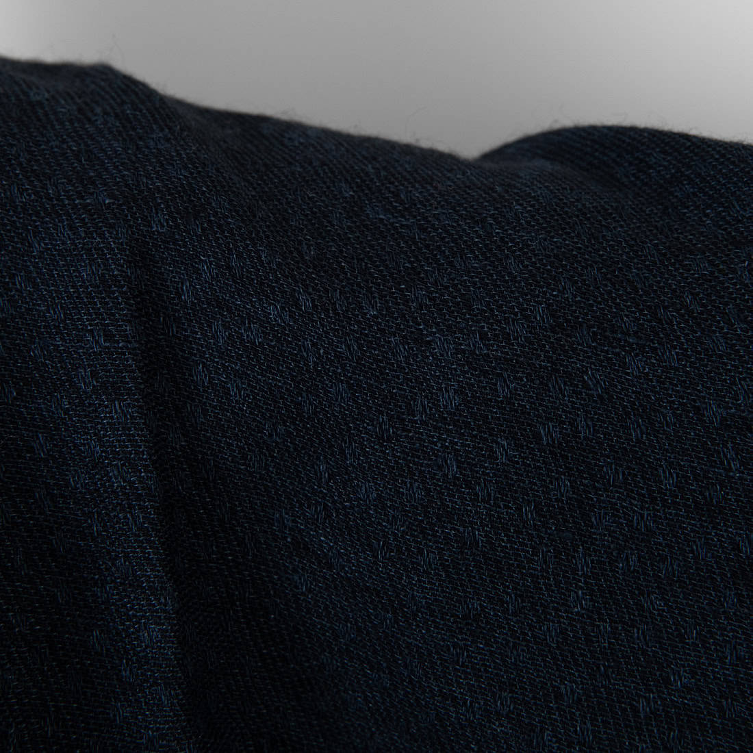 Close-up of a dark navy blue textured fabric with a fine woven pattern, showing soft folds and shadows against a neutral light gray background.