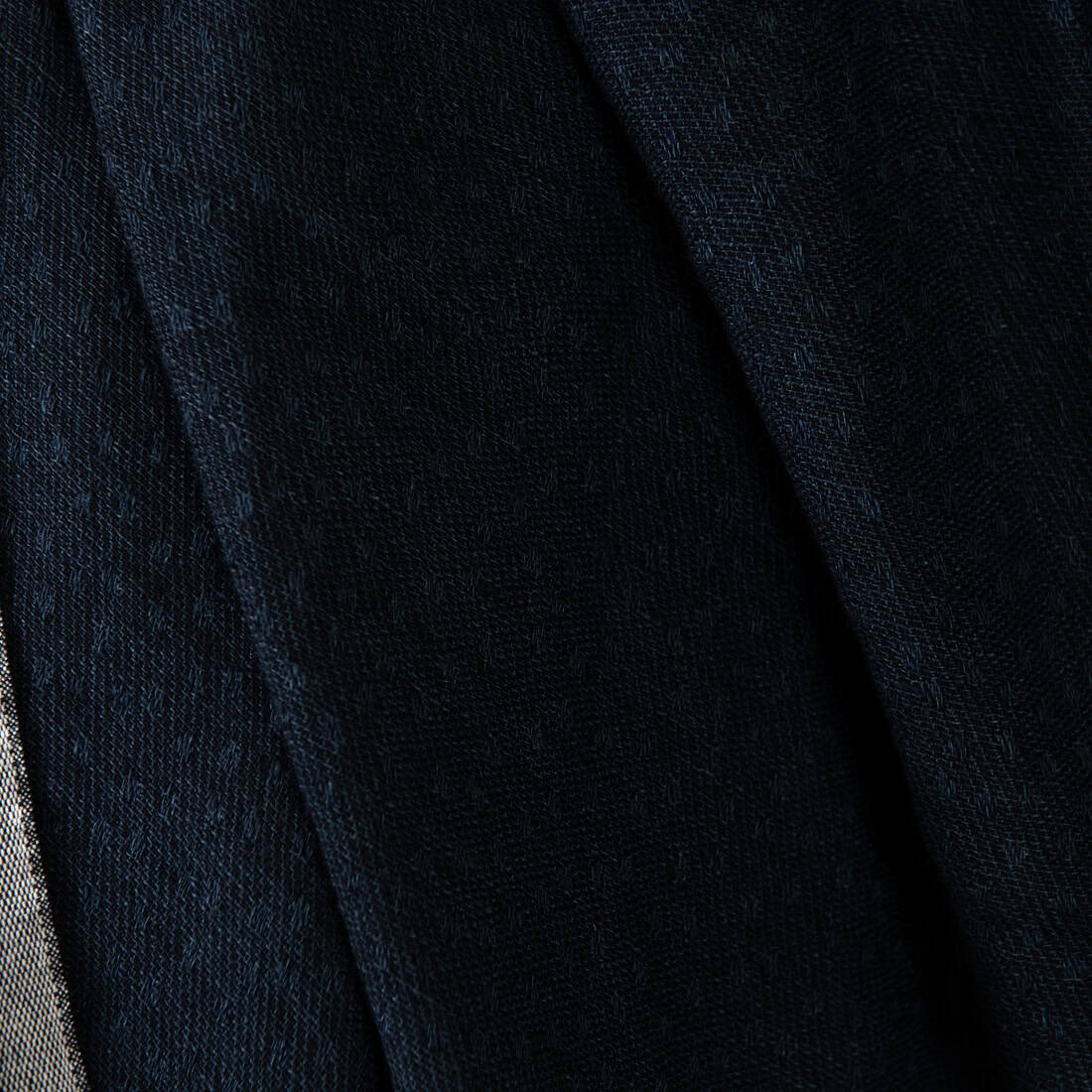 A close-up of dark navy blue textured fabric with soft diagonal folds and a subtle woven pattern.