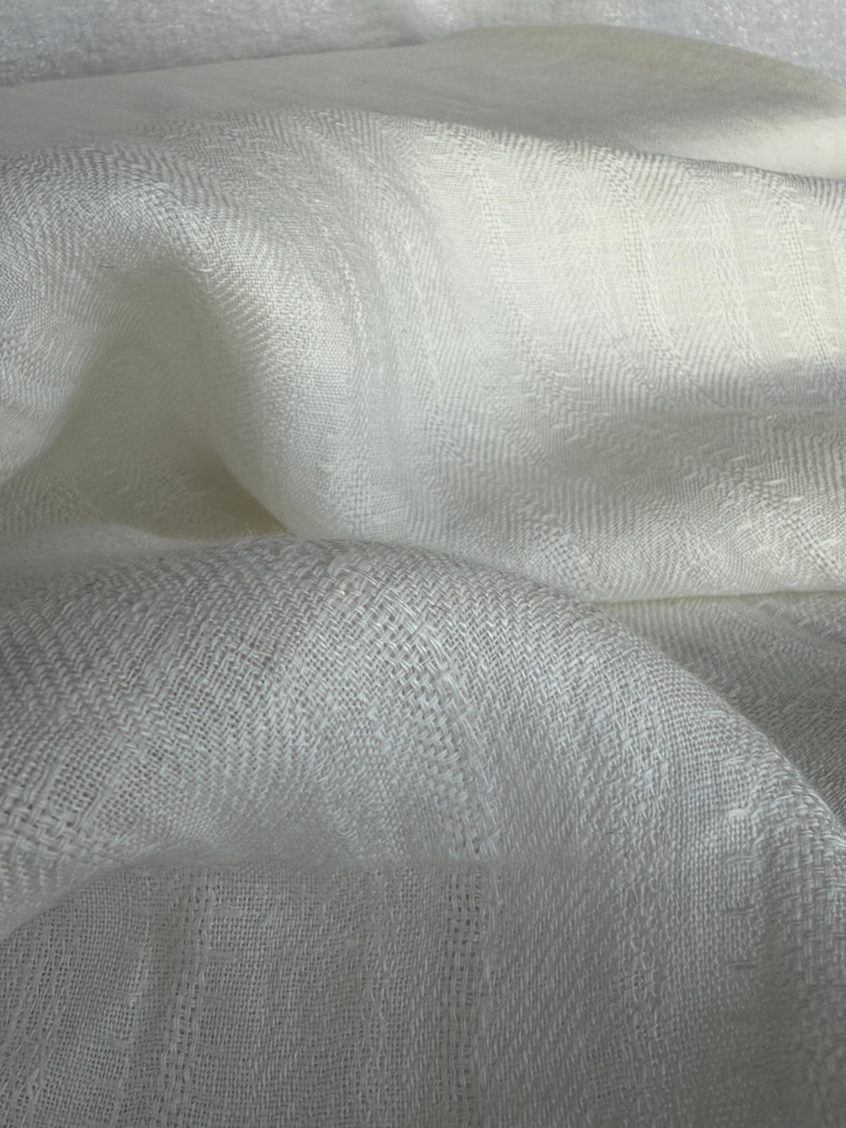A close-up of draped off-white woven fabric with a subtle textured pattern and soft folds.