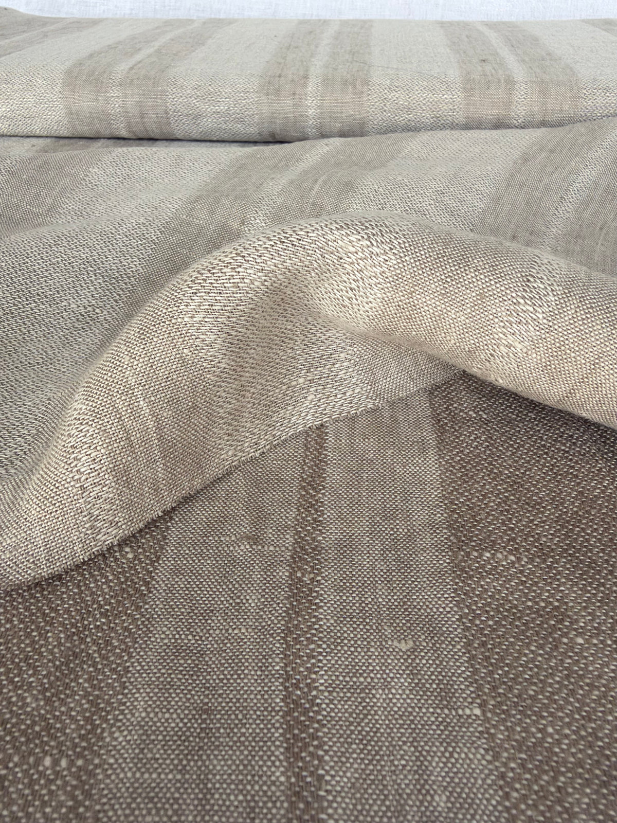 A close-up of a woven textile with a textured, linen-like surface in a warm taupe-beige color, draped to show its soft folds and weave.