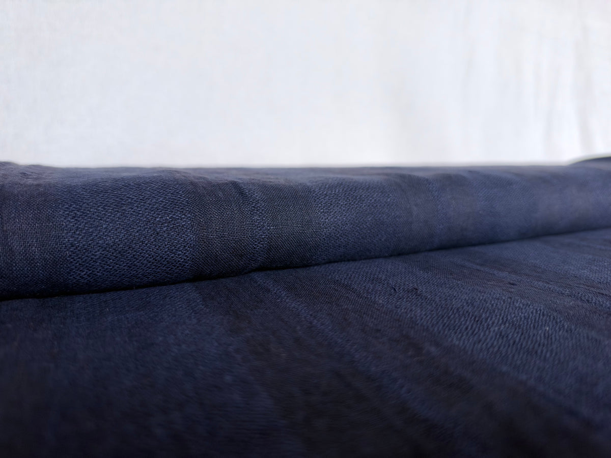 A close-up of dark navy blue fabric, likely linen or a similar textured textile, draped horizontally against a light off-white background.