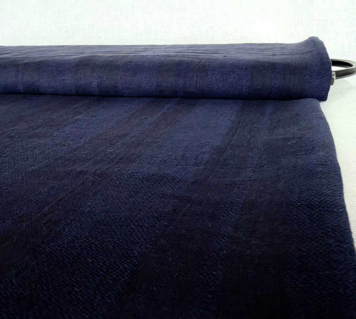 A close-up of a dark navy blue textured fabric, partially rolled, showing its woven texture against a light gray background.