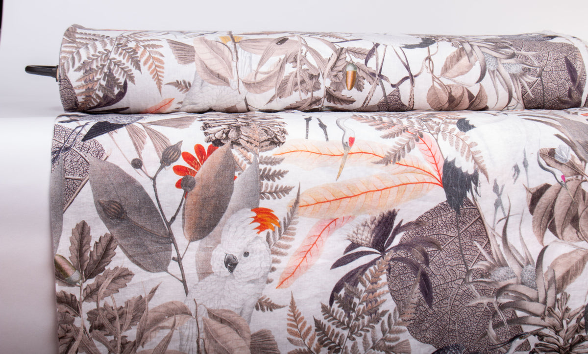 A close-up of a rolled fabric or textile with a botanical and bird print, showing a white base with gray, brown, and orange leafy details and a white cockatoo motif.