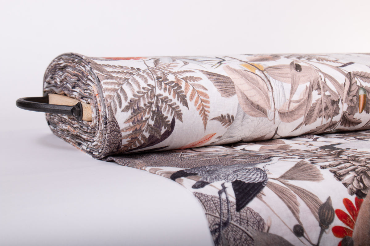 A rolled piece of fabric with a botanical and bird pattern in muted brown, gray, black, and red tones, displayed on a clean white background.