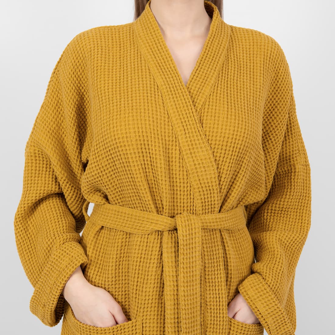 A mustard yellow waffle-knit robe with a matching tie belt and front pockets, shown on a model against a light gray background.