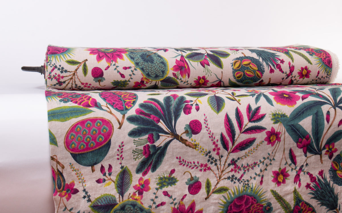 A close-up of a rolled and unrolled fabric with a dense botanical print featuring pink flowers, green and teal leaves, and yellow accents on a light beige background.