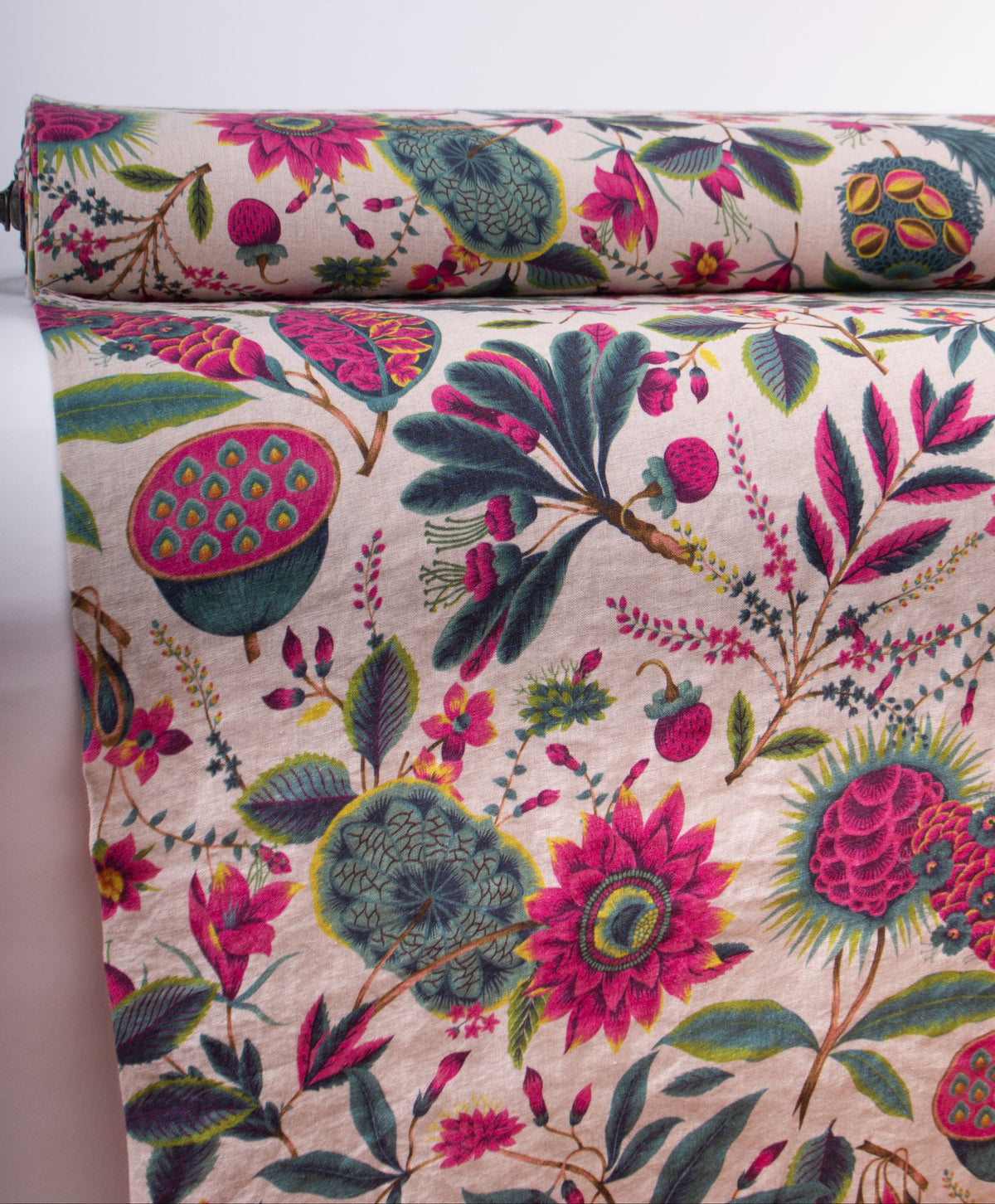 A close-up of a rolled and draped fabric with a dense botanical print featuring pink flowers, green leaves, and lotus pods on a light beige background.