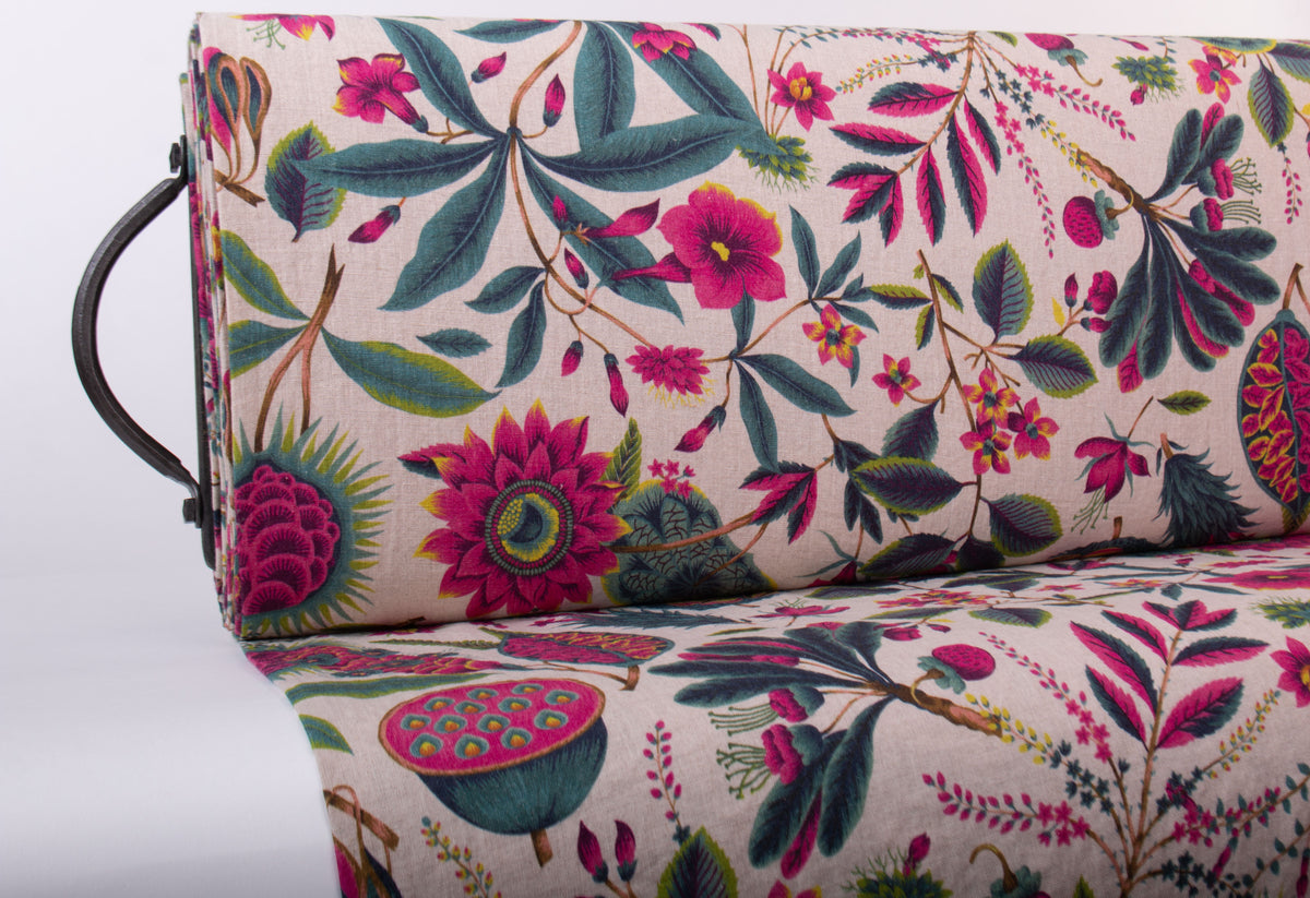 A close-up of upholstered furniture showing a detailed botanical print with pink flowers, green and blue leaves, and fruit motifs on a light beige background. A dark metal side handle is visible on the left.