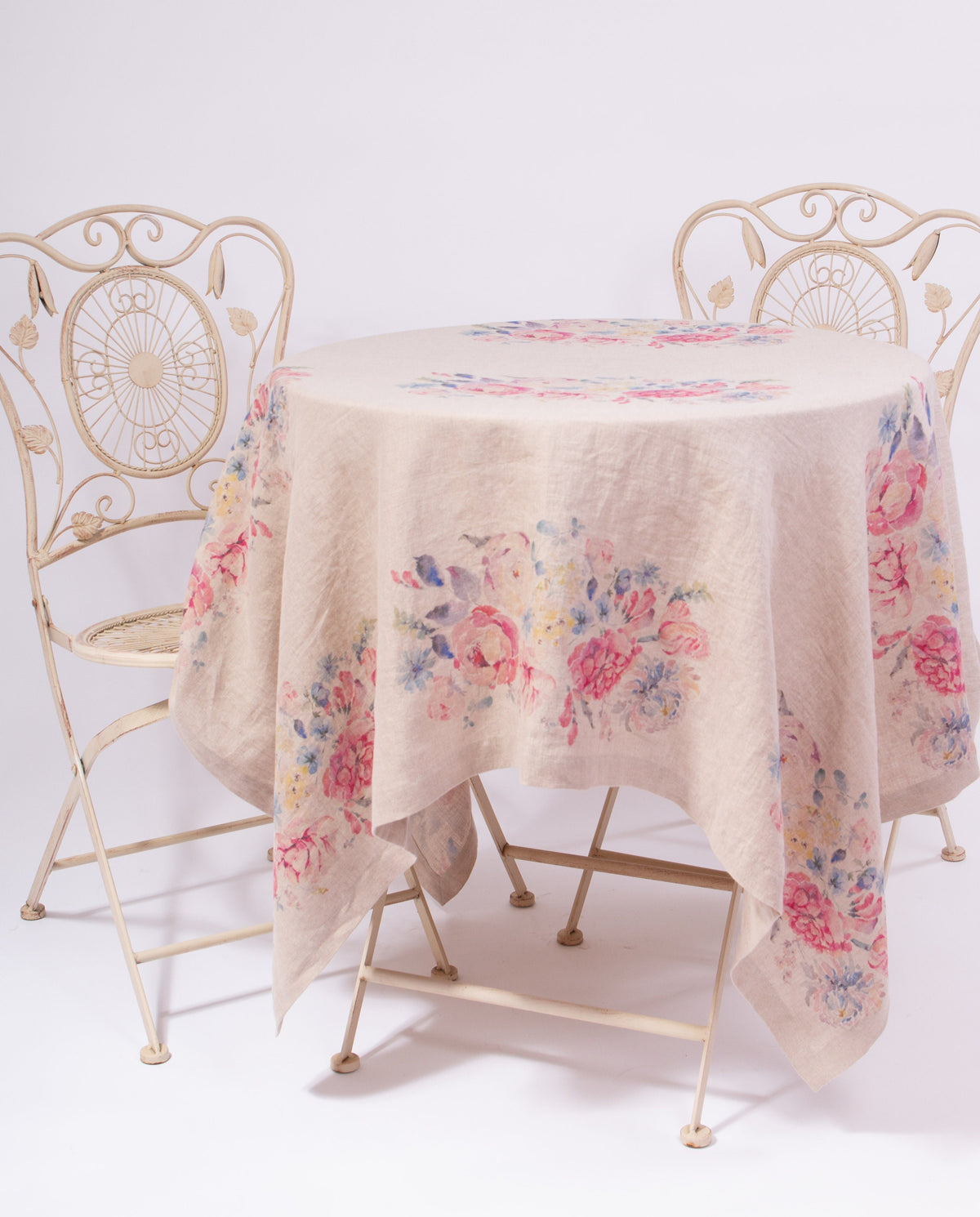 Round table with floral tablecloth and two ornate chairs on a white background