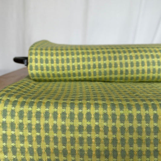 Roll of yellow and green patterned linen fabric spread across a table
