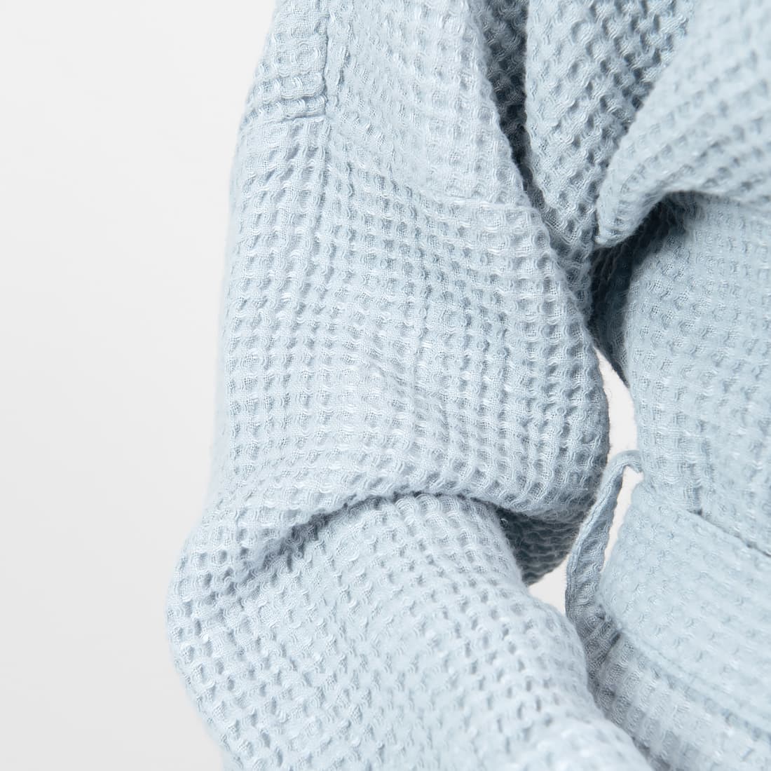 Close-up of a light blue waffle-knit fabric garment, showing the textured knit pattern and soft folds against a plain light background.